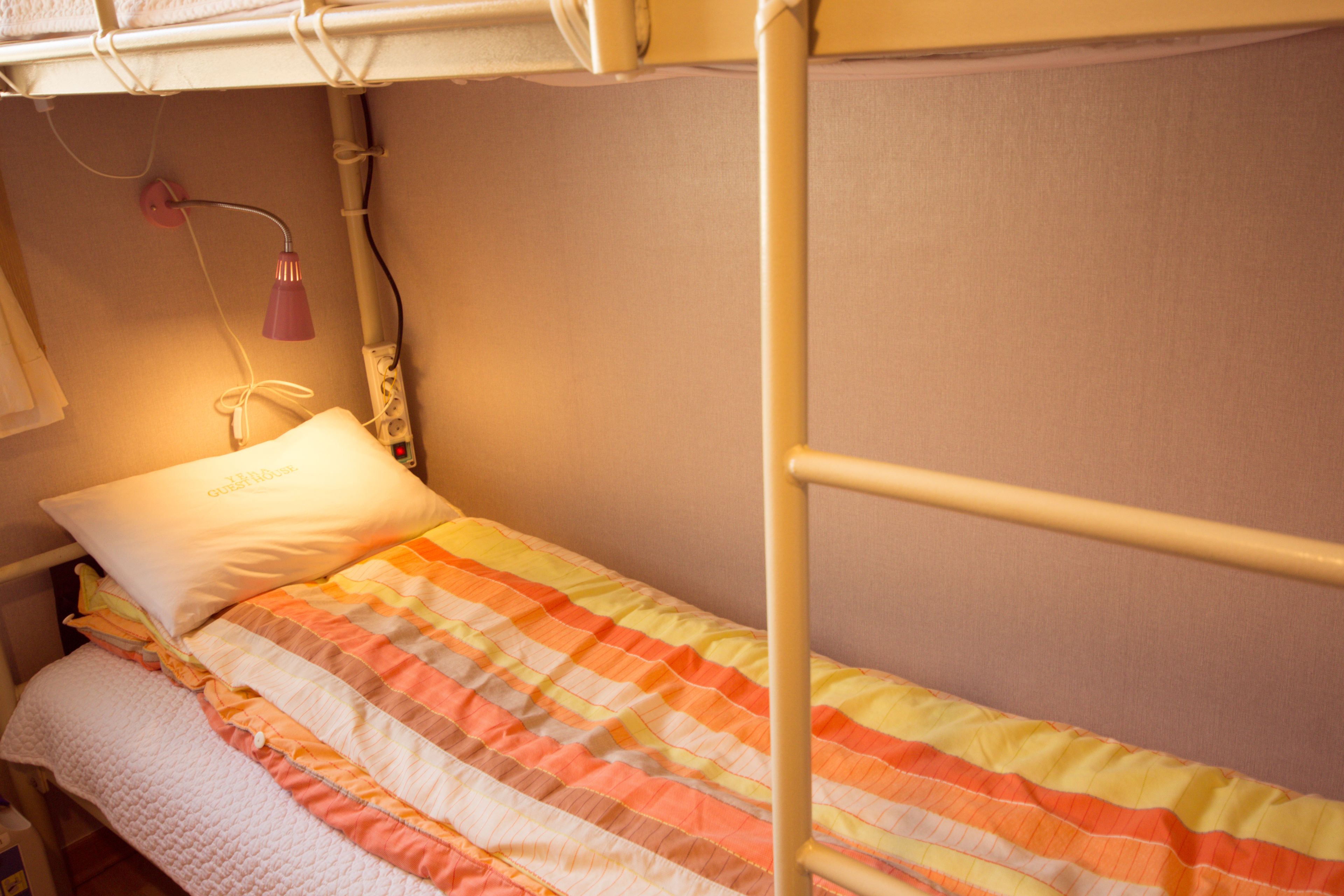 A bunk bed with a striped blanket, a white pillow, and a bedside lamp.