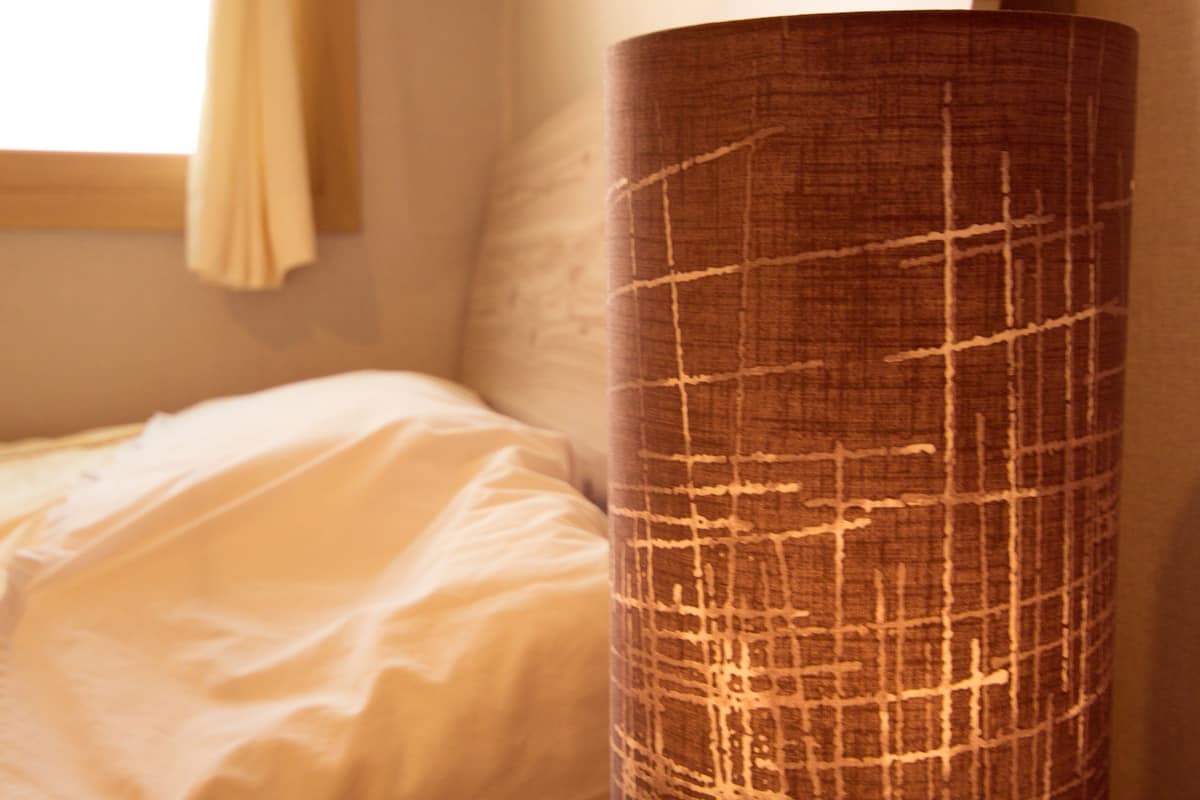 A bed with white bedding, a wooden nightstand, and a cylindrical lamp with a textured surface.