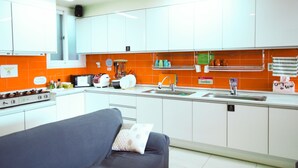 Una cocina moderna con armarios blancos, un salpicadero naranja y un sofá gris en la zona de estar.