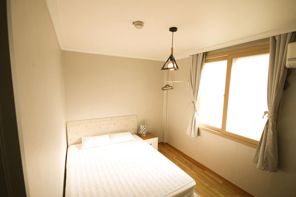 A bedroom with a single bed, a bedside table, a hanging light, and a window with curtains.