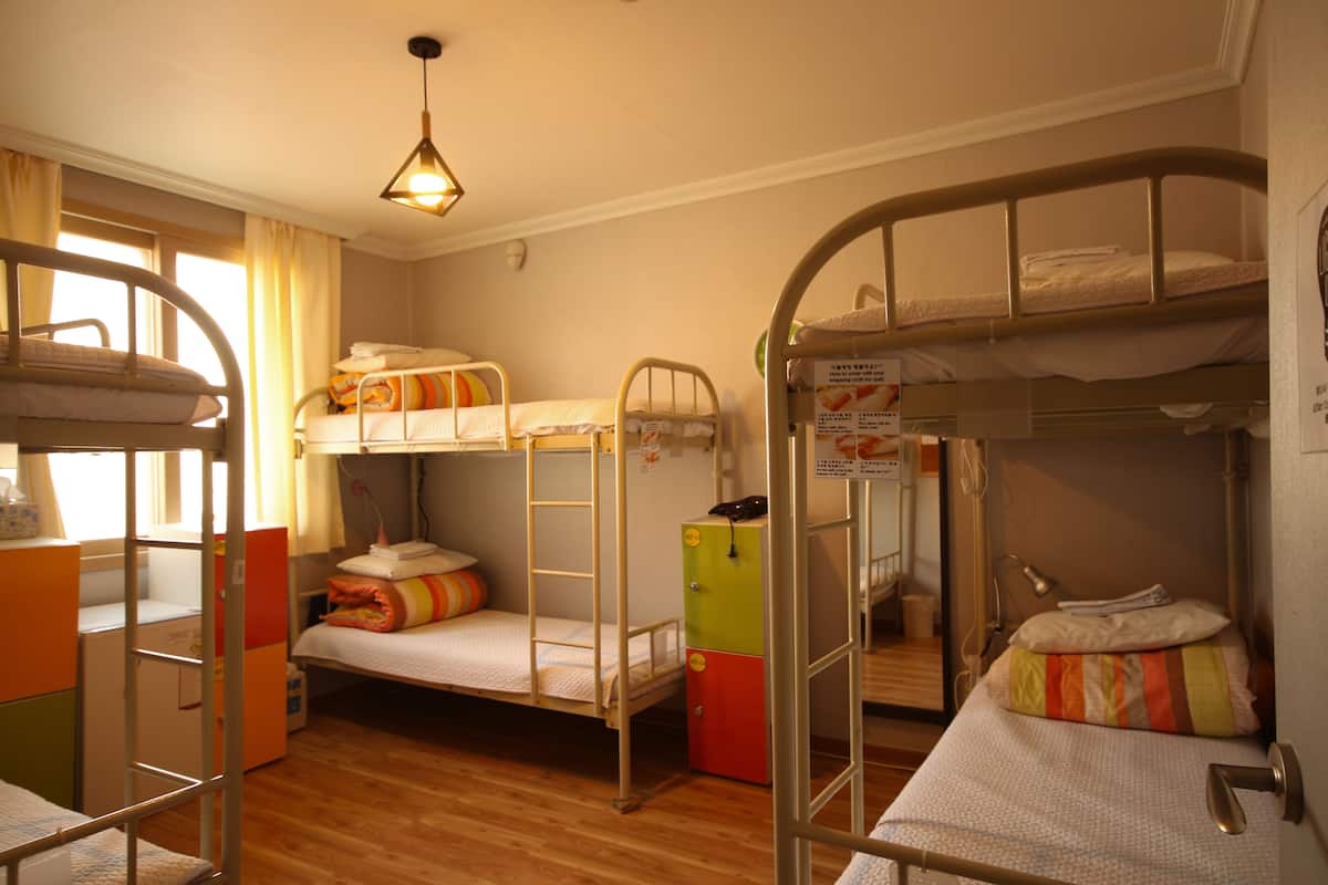 A bunk bed room with a wooden floor, a desk, and a chair.