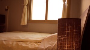 Un dormitorio con cama, ventana con cortinas y una lámpara alta.