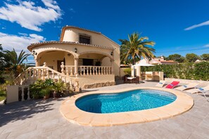 A two-story building with a swimming pool, outdoor seating, and palm trees.