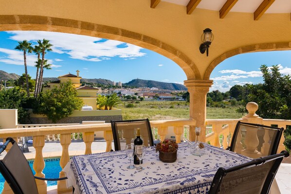 An outdoor patio with a table set for dining, overlooking a scenic landscape with hills and buildings.