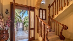 Un escalier en bois, doté d’une rampe courbée, mène à une porte qui donne sur un patio agrémenté de palmiers.