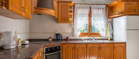 A kitchen with wooden cabinets, a built-in oven, a sink, and a window with curtains.