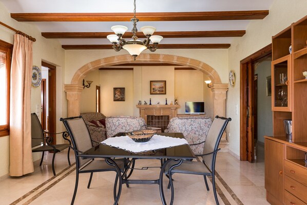 Un comedor con una mesa, sillas, una araña, una chimenea y un televisor.