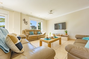 A spacious living room with a beige sofa, a coffee table, and a TV mounted on the wall.