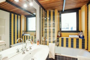 Une salle de bain avec une grande baignoire, un meuble-lavabo avec un miroir et une fenêtre ornée de rideaux à rayures jaunes et noires.