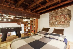 Une pièce comprenant un lit, un baby-foot, une bibliothèque et une tapisserie.