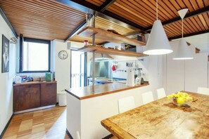 Une cuisine moderne avec des meubles en bois, une table à manger en bois, des luminaires suspendus et une vue sur la salle à manger adjacente.