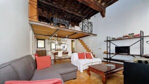 A spacious living room with a sofa, ottoman, and a coffee table. A staircase leads to an upper level with a balcony. - Rome, historic center, characteristic apartment for 6 (Roma)