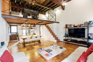 Un espace de vie moderne de style loft, comprenant un coin repas, un escalier et un téléviseur posé sur une étagère.