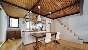 A modern kitchen with wooden flooring, a dining area with a wooden table and white chairs, and a staircase with wooden steps. - Rome, historic center, characteristic apartment for 6 (Roma)
