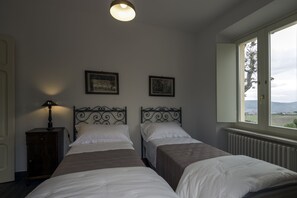 Une chambre avec deux lits simples, une table de chevet avec une lampe et une fenêtre donnant sur l’extérieur.