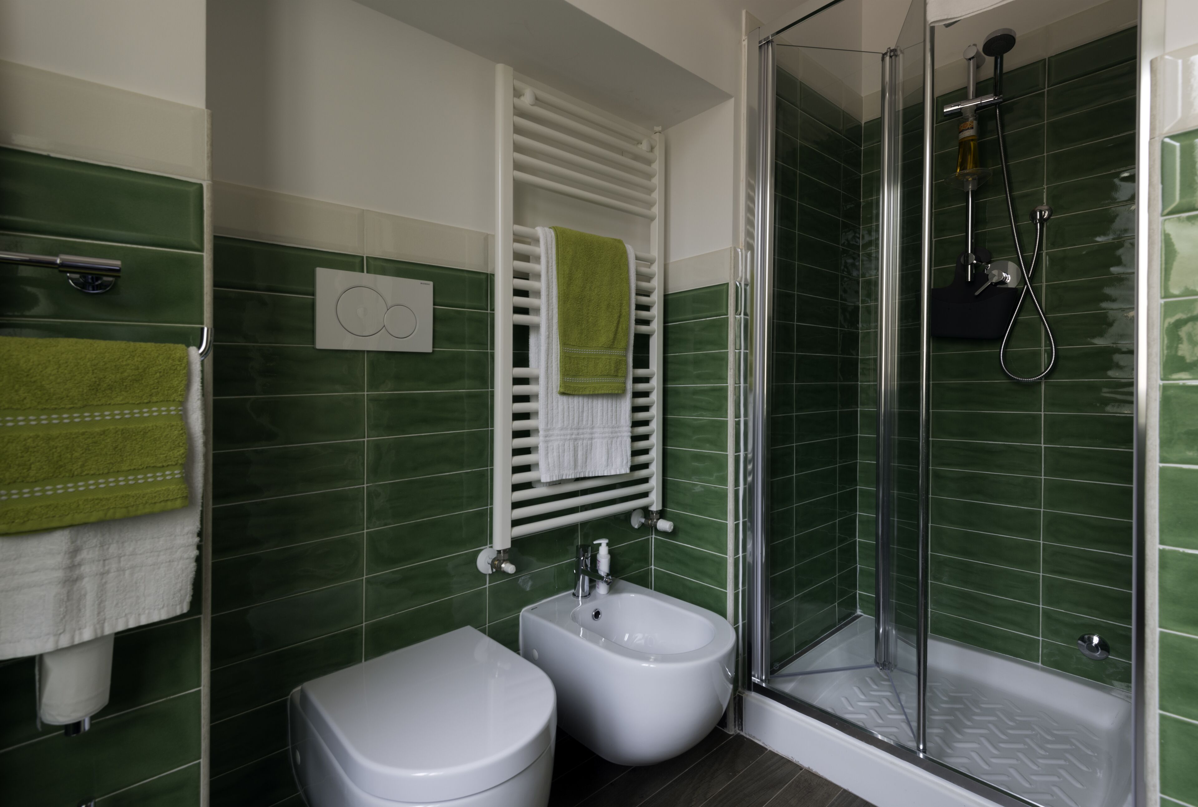 Ein Badezimmer mit grünen Fliesen, einer weißen Toilette, einem Bidet, einer Duschkabine und zwei Handtüchern an Handtuchhaltern.