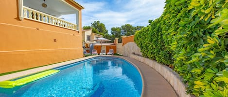 Une piscine à l’eau d’un bleu limpide, entourée d’un petit muret en pierre et d’une haie bien entretenue.