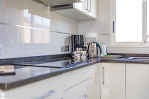 A modern kitchen with white cabinets, a black countertop, a coffee maker, and a kettle.