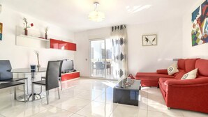 A modern living room with a red sofa, a glass dining table, and a TV.