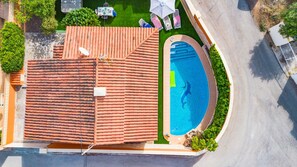 A rooftop swimming pool with a tiled roof, surrounded by greenery and a paved area.