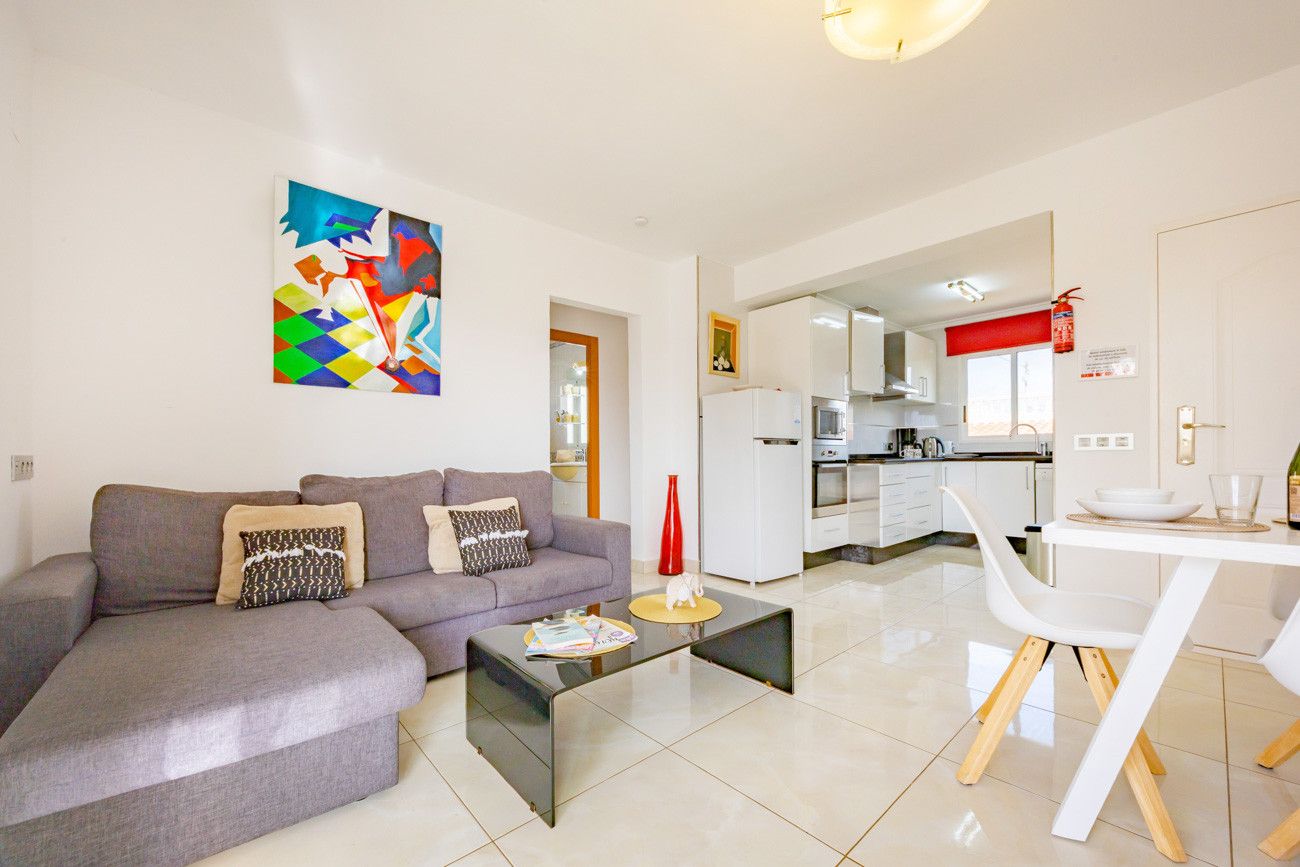 A modern living room with a gray sofa, a coffee table, and a dining area with a white table and chairs.