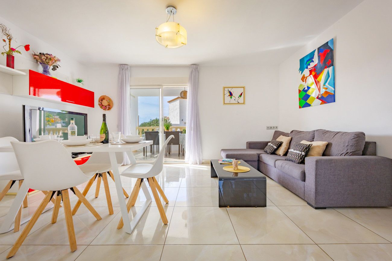 A modern living room with a grey sofa, white chairs, a dining table, and a TV.