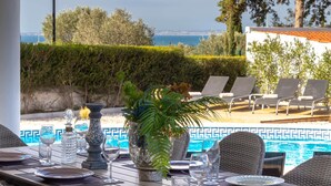A dining table set with glassware and a decorative vase, overlooking a swimming pool and lounge chairs. - Villa Ocean Blue, Ocean views , Walk to beach, Pool (Ferragudo)