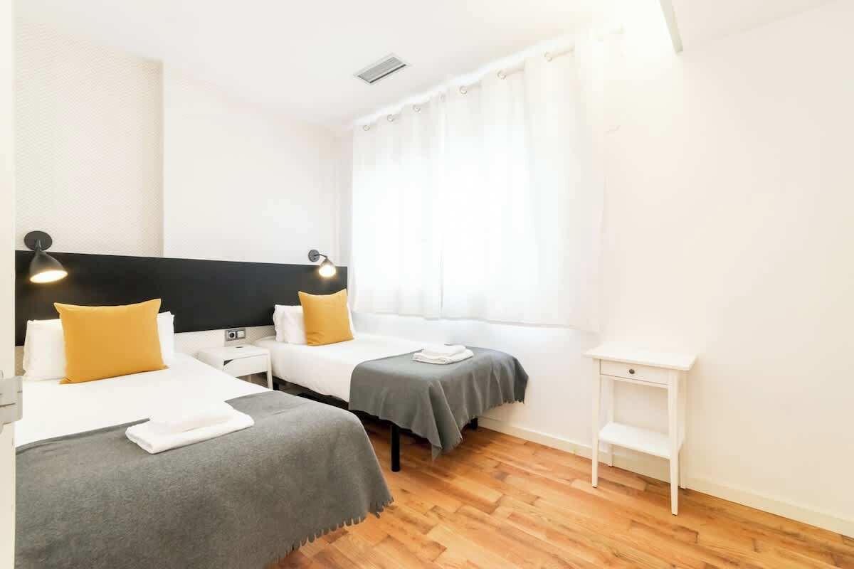 Una camera d'albergo con due letti, un comodino e una finestra con tende.