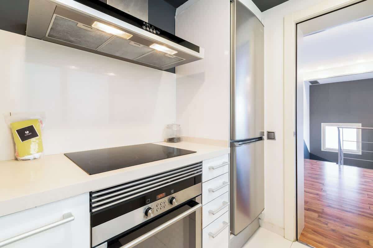 Een moderne keuken met een roestvrijstalen koelkast, een zwart inductiekookplaatje en witte kastjes.