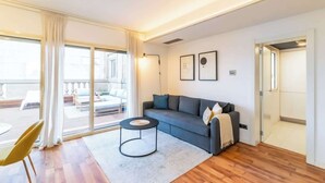 A modern living room with a grey sofa, a round coffee table, and a large sliding glass door leading to an outdoor seating area. - Central Penthouse with terrace Plaça Catalunya I (Barcelona)