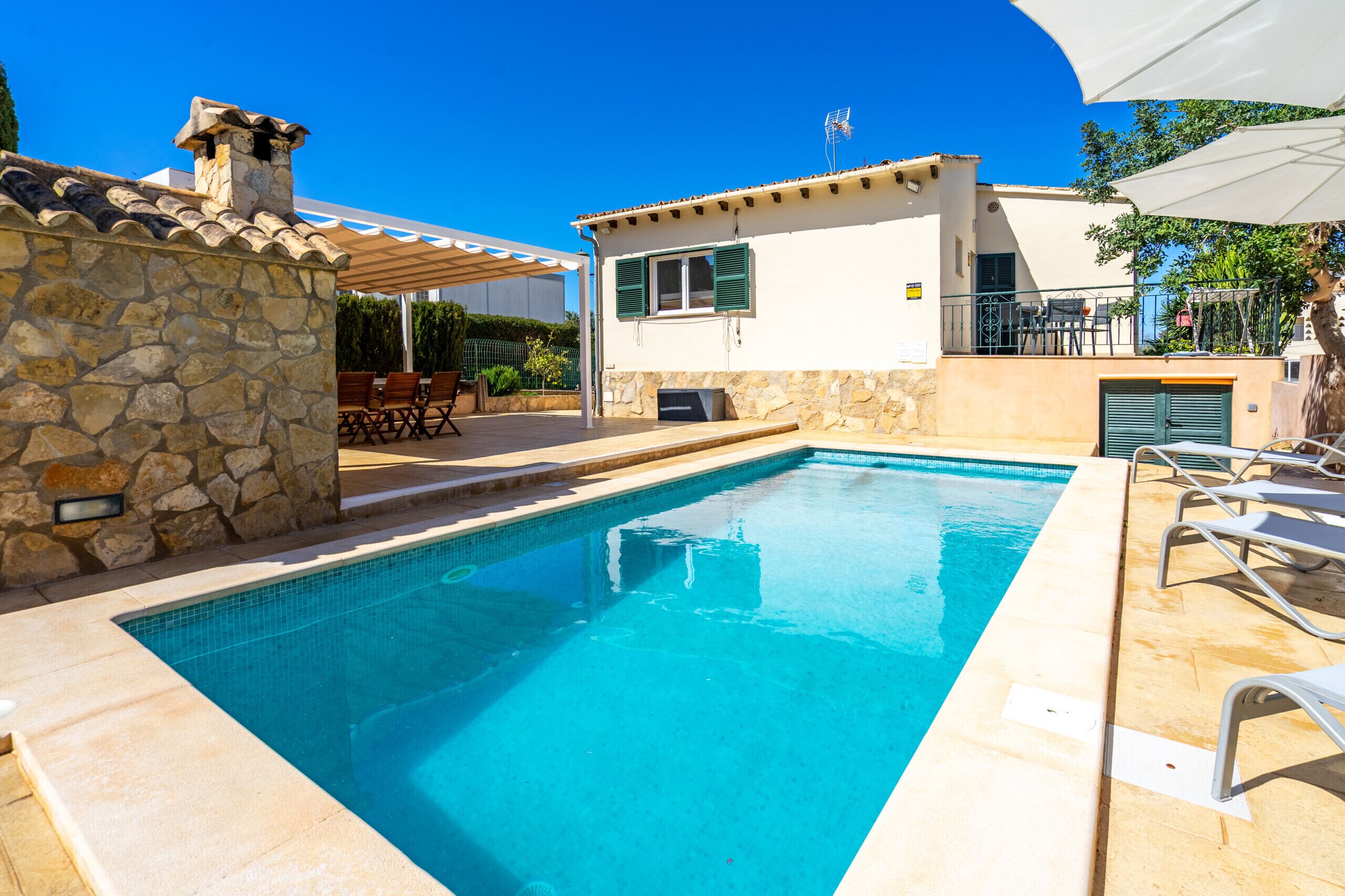 A swimming pool with a stone wall, a covered patio, and a small building with a balcony.
