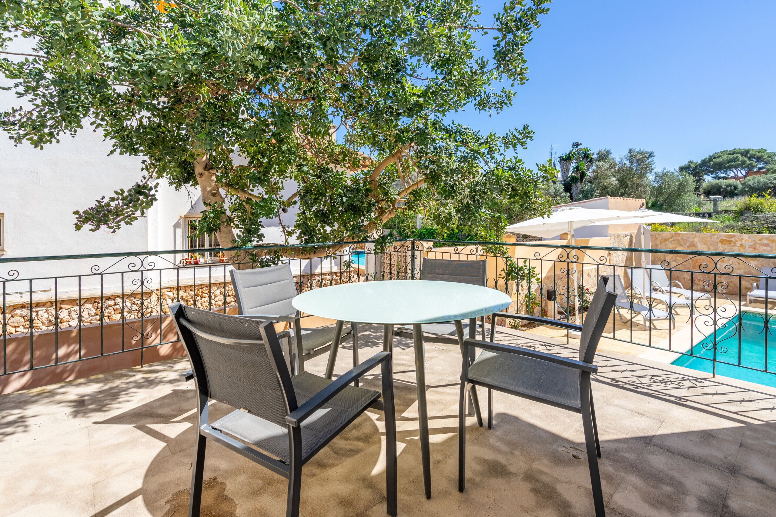 Une terrasse extérieure avec une table ronde et des chaises, une piscine et un arbre qui offre de l’ombre.