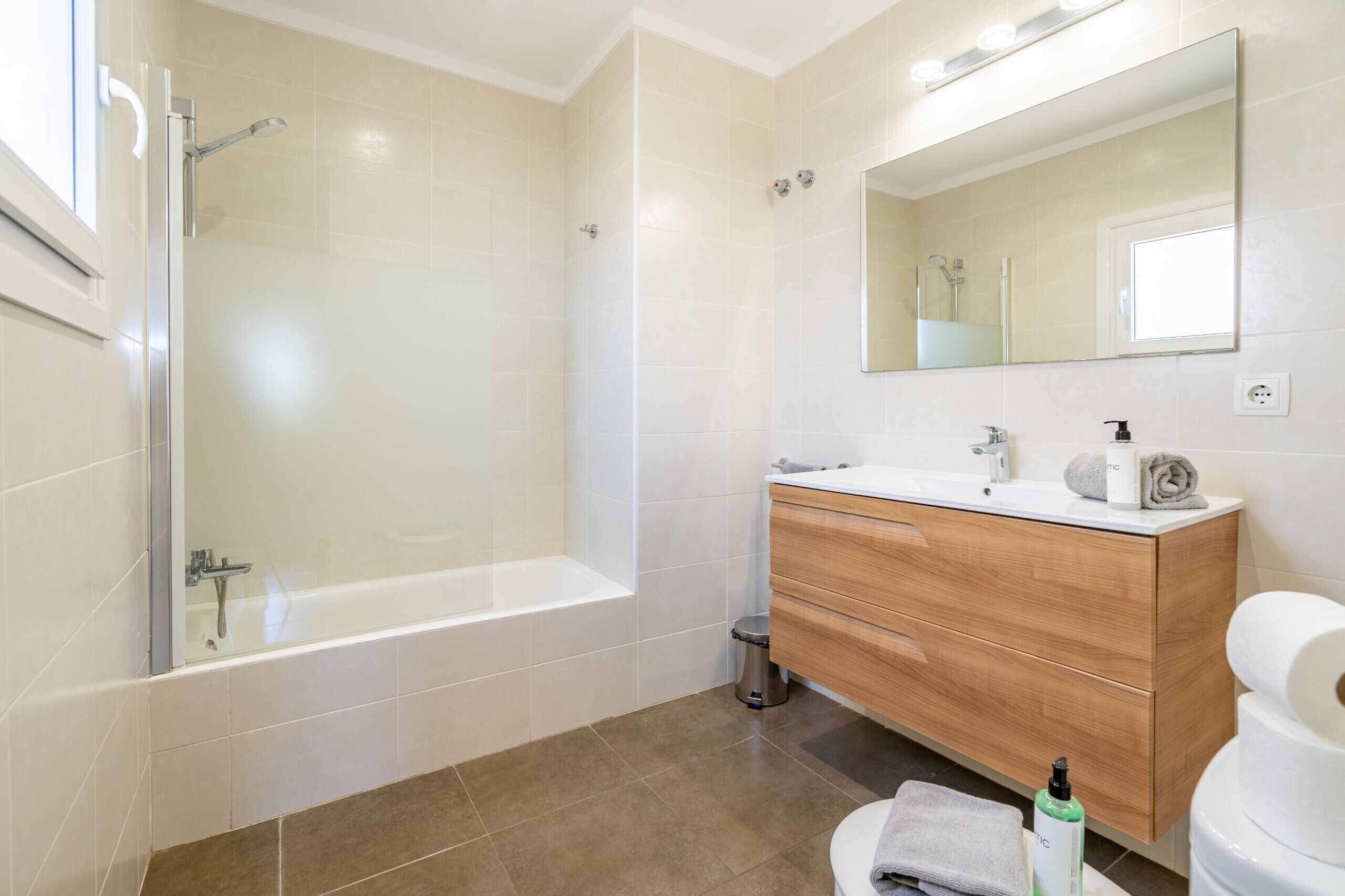 A modern bathroom with a bathtub, vanity, mirror, and toilet.