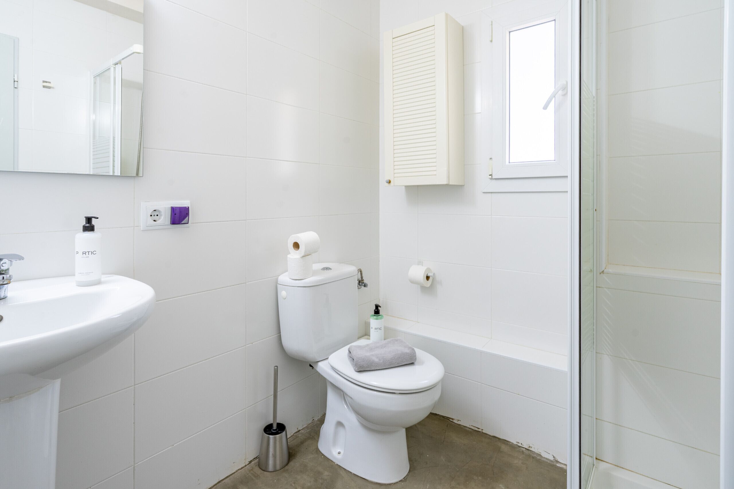 A bathroom with a white sink, toilet, and bidet, a mirror, and a window with a shutter.