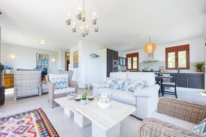 A spacious living area with a sofa, chairs, a coffee table, and a kitchen in the background. - Villa Lia - PlusHolidays (Calpe)