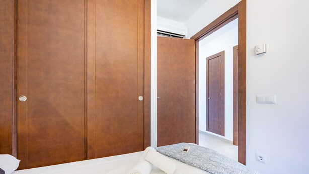 A bedroom with a bed, a wooden wardrobe, and a hallway leading to another room. - Villa Lia - PlusHolidays (Calpe)
