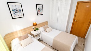A hotel room with two beds, a nightstand, a lamp, a framed picture of Paris, a framed picture of London, and a wooden door. - Apartment with parking near PortAventura (Salou)