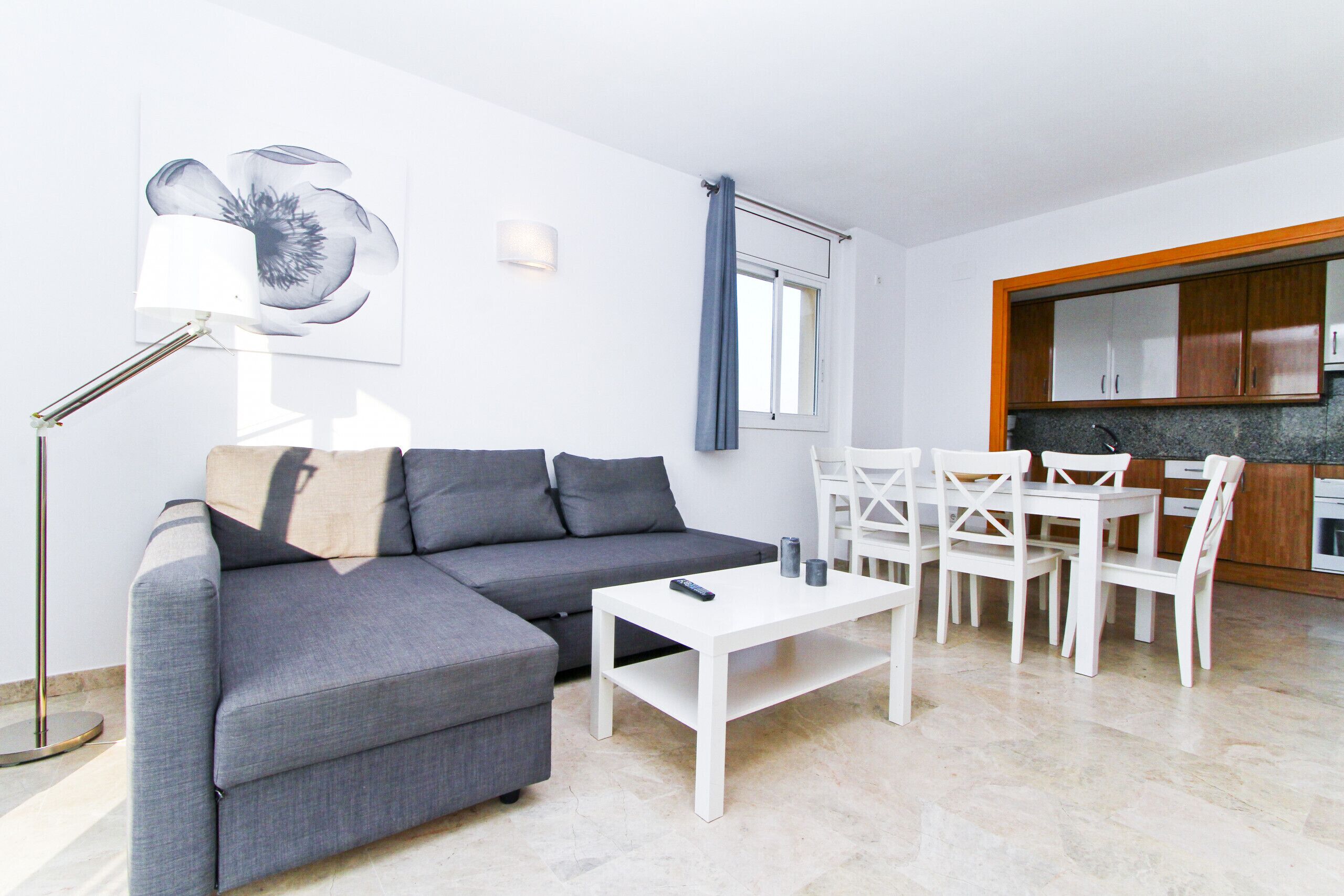 A modern living room with a grey sofa, white coffee table, and dining area with white chairs.