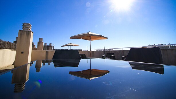 A clear blue sky with a sun shining, a reflective pool, and two umbrellas. - Apartment with parking near PortAventura (Salou)