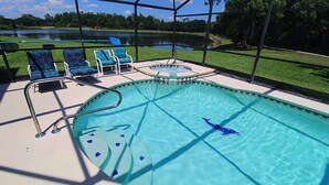 A swimming pool with a hot tub, lounge chairs, and a view of a lake.