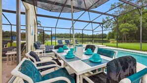A covered outdoor dining area with a pool view, white tables, and blue chairs.