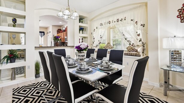 A dining area with a chandelier, black and white chairs, and a table set for four.
