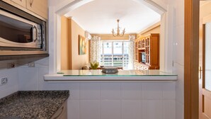 A kitchen with a built-in microwave, a glass-top island, and a view of the dining area through an arched doorway. - CARLOS V Apartment (Salou)