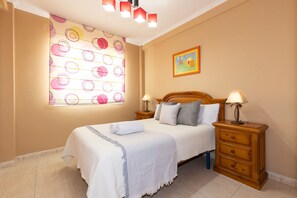 Une chambre à coucher avec un lit, deux tables de chevet avec des lampes, une fenêtre ornée de motifs circulaires et un tableau accroché au mur.