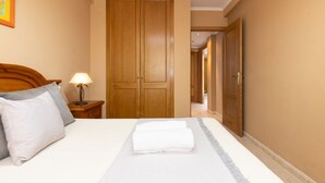 A hotel room with a bed, a nightstand with a lamp, a wooden wardrobe, and a door leading to another room. - CARLOS V Apartment (Salou)