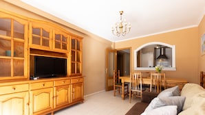 A living room with a wooden entertainment center, a flat-screen TV, a dining area with a table and chairs, and a sofa. - CARLOS V Apartment (Salou)