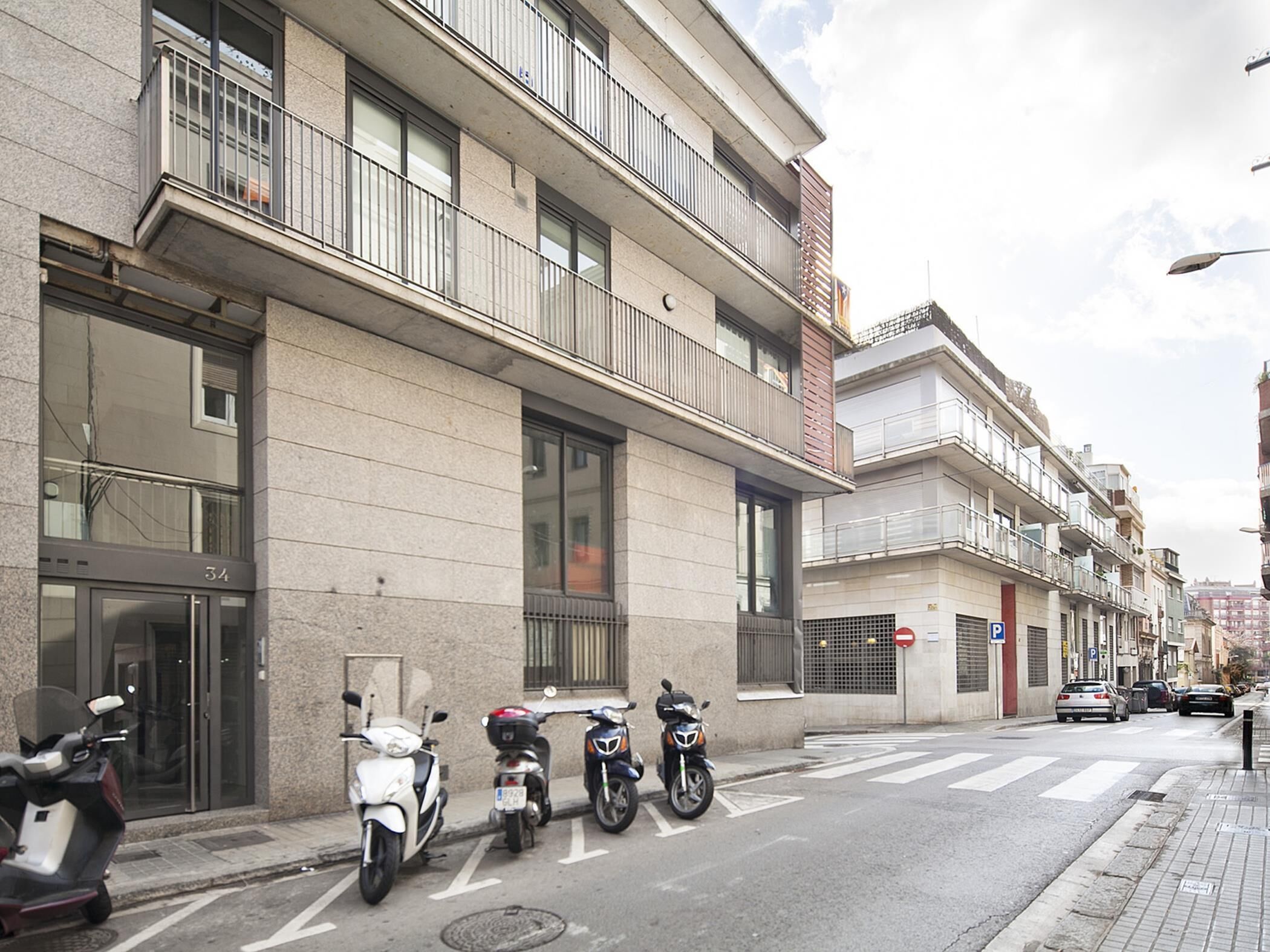 Un edificio moderno con ingresso a livello strada, un'area di parcheggio e diversi scooter parcheggiati.
