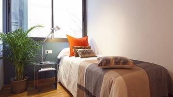 Un dormitorio con cama, mesita de noche, lámpara, planta en maceta y ventana.