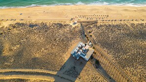 An aerial view of a beach resort with a central building surrounded by a sandy area, a pathway leading to the beach, and a row of beach chairs. - Villa w/ private pool & BBQ in Varandas do Lago (Almancil)