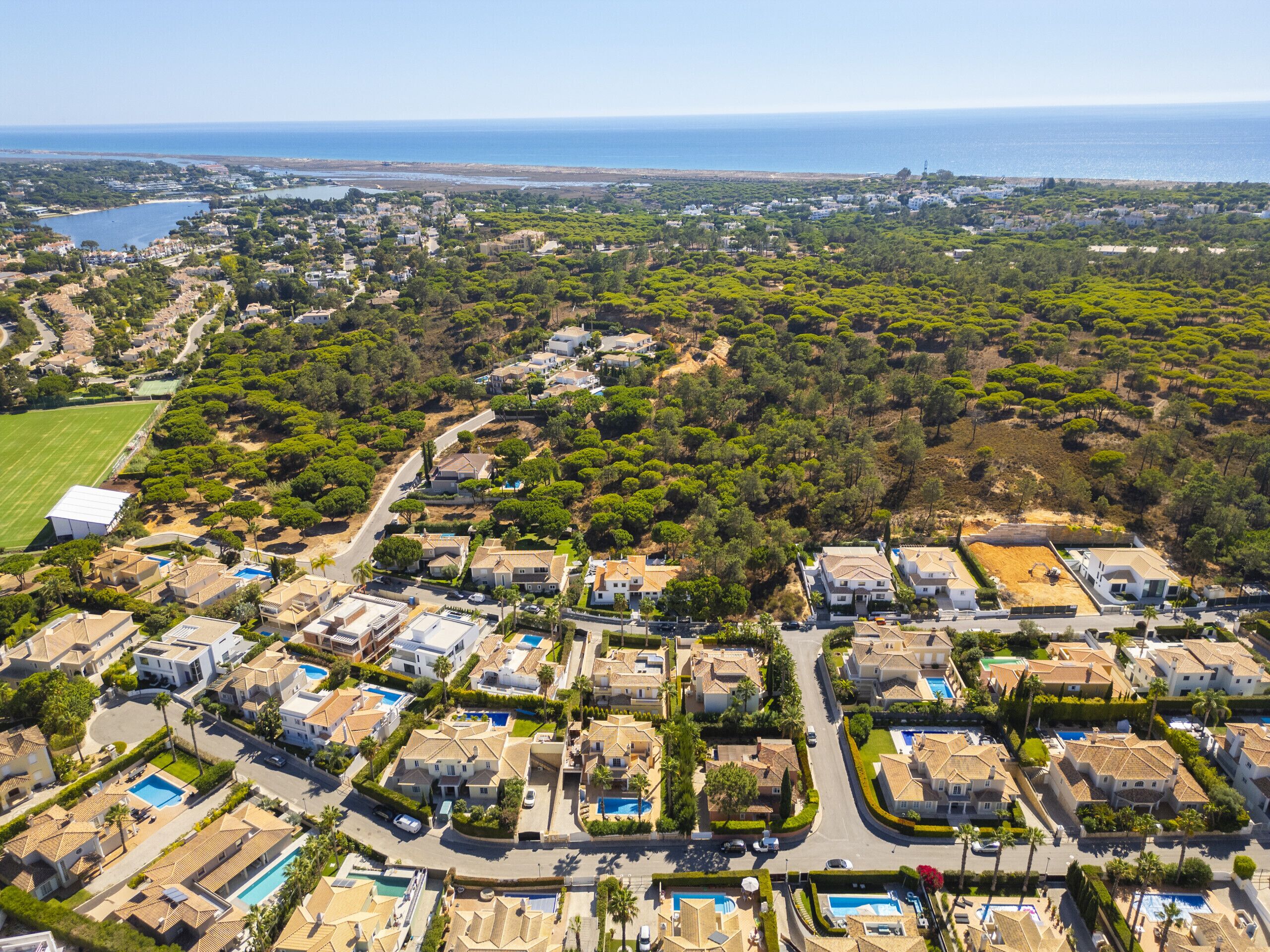 An aerial view of a coastal residential area with houses, roads, and a beach in the background.